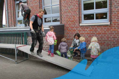 Kinder bepflanzen das Dach des Kellerzugangs der Kita "Raupe Nimmersatt" in Overhetfeld. Daneben zwei Erwachsene, die die Arbeiten betreuen.