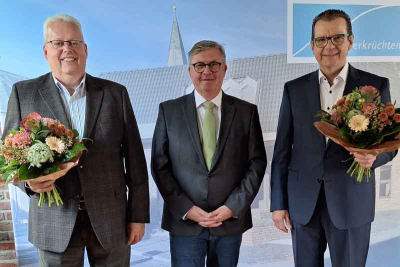 Matthias Dumpf, Bürgermeister Karl-Heinz Wassong, Jörg Sahlmann vor einer Wand mit dem Bild des Rathauses in Elmpt. Die Personen links und rechts mit einem Blumenstrauß in der Hand.