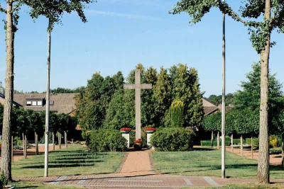Ein Kreuz auf dem Friedhof in Niederkrüchten. Im Vordergrund ein darauf zulaufender Weg und Bäume.