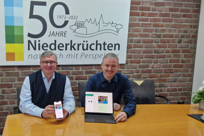 Bürgermeister Karl-Heinz Wassong und Wirtschaftsförderer Frank Grusen mit einem Smartphone und einem Tablet, auf denen der WhatsApp Kanal der Gemeinde Niederkrüchten geöffnet ist