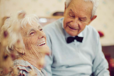 Ein älterer Mann und eine Frau lachen. Er blickt sie von der Seite an.