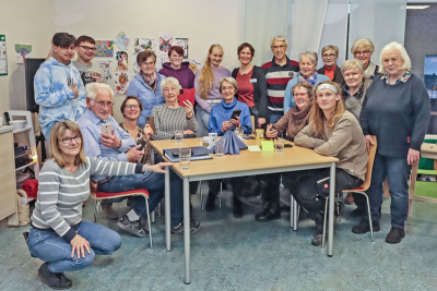 Teilnehmerinnen und Teilnehmer sowie Organisatorinnen und Organisatoren des Handytreff in Niederkrüchten an einem Tisch. Einige halten ein Smartphone in der Hand.