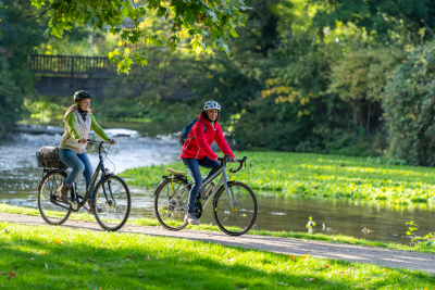 Zwei Fahrradfahrerinnen vor einem Fluß mit einer Brücke.