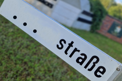 Ein Schild mit der Aufschrift "...Straße". Im Hintergrund unscharf der Zufahrtsbereich des künftigen Gewerbe- und Industriepark Elmpt