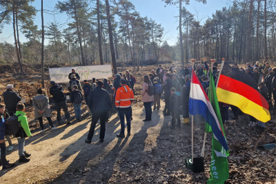 Bürgermeister Karl-Heinz Wassong hält eine Ansprache zum Baumpflanztag im Elmpter Wald. Im Hintergrund ein Banner mit der Aufschrift "Bäume kennen keine Grenzen - bomen kennen geen grenzen". Im Vordergrund Kinder und Erwachsene, die zuhören sowie eine niederländische und eine deutsche Flagge.