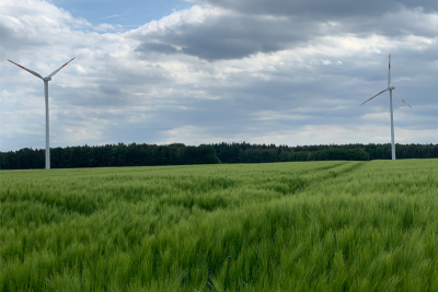 Zwei Windräder vor bewölktem Himmel.