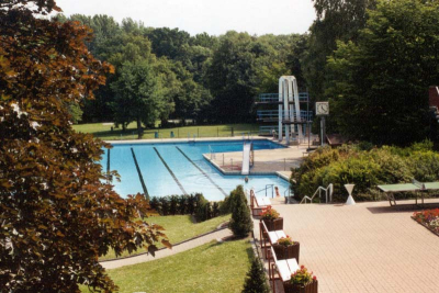 Blick auf das Freibad Niederkrüchten. Im Hintergrund ein Schwimmbecken mit Sprungturm und Uhr.