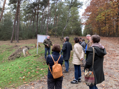 Eine Personengruppe steht im herbstlichen Wald vor einer Informationstafel.