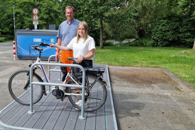 Mike Langenbahn, Leiter des Bauhofs, und Klimaschutzmanagerin Lea Korall stehen mit einem Fahrrad auf der Fahrradflunder am Lindbruch. Im Hintergrund eine Radbox zum Einschließen von Fahrrädern.